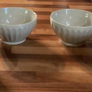 Puede incluir: Cuatro cuencos de cerámica verde claro con un diseño acanalado en el exterior. Los cuencos están colocados sobre una superficie de madera. Estos cuencos tienen un diseño sencillo y elegante, adecuado para servir varios platos.