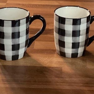 May include: A white ceramic mug with a black handle and the text "But first, coffee" in a handwritten style. The mug is on a white surface. The mug is approximately 4 inches tall.