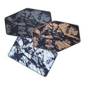 May include: A collection of four hexagonal coasters with a marbled design. The coasters feature a mix of colors, including black, gray, white, and tan. Each coaster has a unique pattern, adding visual interest. The coasters are likely made of a durable material.
