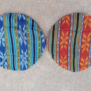 May include: Two round, patterned cushions with a quilted design. One cushion is blue, green, and white, and the other is red, orange, and yellow.