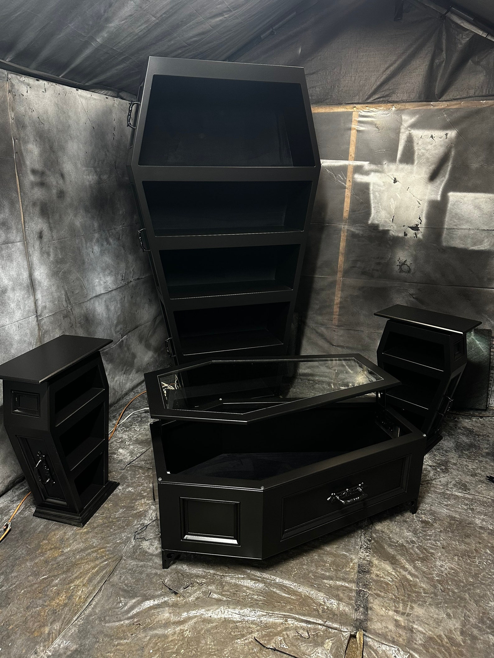 Unlit black coffin furniture set featuring a tall bookshelf, two matching side tables, and a coffin coffee table with glass lid