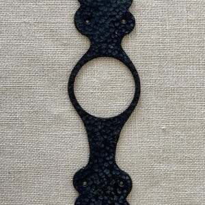 Puede incluir: Un llamador de puerta de metal negro con un acabado texturizado y un diseño de media luna. El llamador tiene una abertura circular para el pomo de la puerta.