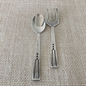 May include: A set of silver-plated cutlery with a geometric design. The spoon and fork have a black and white pattern on the handle.