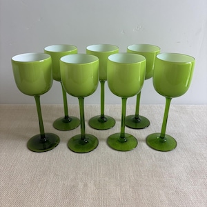 Puede incluir: Un conjunto de siete copas con tallo que presentan cuencos de color verde lima brillante con interiores blancos y tallos y bases circulares de color verde oscuro. Las copas están dispuestas en dos filas, mostrando un diseño uniforme.