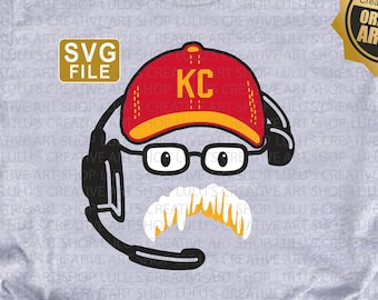 May include: A grey t-shirt featuring a cartoon illustration of a person wearing a red and white baseball cap with the letters "KC" on it. The person is wearing glasses and a moustache. The illustration is surrounded by a black circle and a headset.