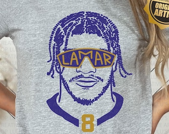 May include: A grey t-shirt featuring a purple and gold illustration of a football player wearing sunglasses. The player's name "LAMAR" and number "8" are visible on the shirt. The text "LULU'S Creative ArtShop ORIGINAL ARTIST" is on a gold star sticker.