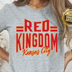 May include: A gray t-shirt with the text "=RED= KINGDOM Kansas City" in red and yellow lettering. The shirt is being worn by a person. A gold star sticker with the text "LULU'S Creative ArtShop ORIGINAL ARTIST" is in the upper right corner of the image.