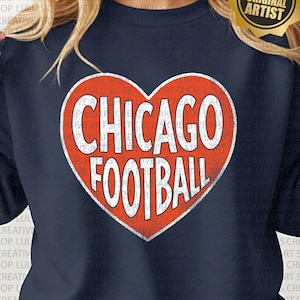 May include: Navy blue sweatshirt featuring a distressed red heart with the words "CHICAGO FOOTBALL" in white. The sweatshirt has a crew neck and long sleeves. A gold sticker with the text "LULU'S CreativeArtShop ORIGINAL ARTIST" is on the upper right.