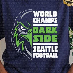 以下が含まれることがあります： 緑と白のワシのグラフィックと「WORLD CHAMPS DARK SIDE SEATTLE FOOTBALL」の文字が入ったネイビーブルーのTシャツ。シャツには「SVG/PNG」の文字も入っています。