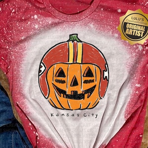 May include: Red and white tie-dye t-shirt featuring a pumpkin wearing a football helmet. The pumpkin has a carved face and is orange with a red and yellow helmet. The text "Kansas City" is below the pumpkin.