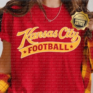 May include: A red short-sleeved t-shirt featuring the yellow text Kansas City FOOTBALL in a curved banner design with two stars. The shirt is worn under a yellow and red plaid long-sleeved shirt. A gold badge with black text is visible.