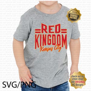 May include: A gray t-shirt with the text "=RED= KINGDOM Kansas City" in red and orange lettering. The shirt is being worn by a child.