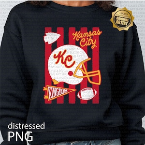 May include: A black long-sleeve sweatshirt featuring a graphic print with red vertical stripes, a white football helmet with the letters KC in red, a red pennant with the word KINGDOM, a football, and the text Kansas City in yellow script.