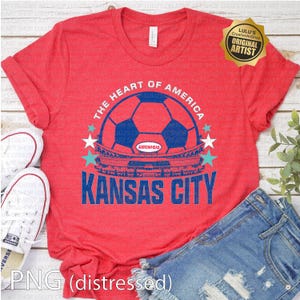 Puede incluir: Camiseta roja con un gr&aacute;fico azul y blanco. El gr&aacute;fico incluye un bal&oacute;n de f&uacute;tbol, las palabras "The Heart of America" y "Kansas City", y una ilustraci&oacute;n de un estadio. La camiseta se combina con pantalones cortos de mezclilla y zapatillas blancas.