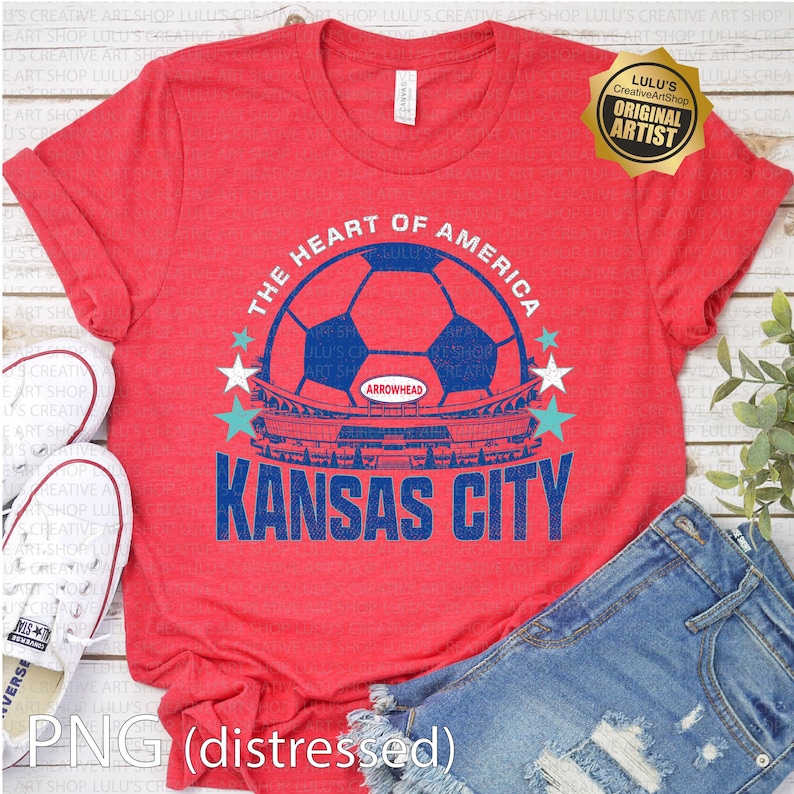 Puede incluir: Camiseta roja con un gr&aacute;fico azul y blanco. El gr&aacute;fico incluye un bal&oacute;n de f&uacute;tbol, las palabras "The Heart of America" y "Kansas City", y una ilustraci&oacute;n de un estadio. La camiseta se combina con pantalones cortos de mezclilla y zapatillas blancas.