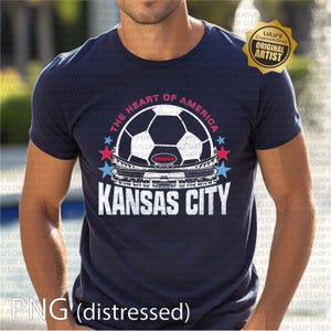 Puede incluir: Camiseta azul marino con un dise&ntilde;o de bal&oacute;n de f&uacute;tbol, el texto "The Heart of America" y "Kansas City". El dise&ntilde;o incluye estrellas rojas y azules y una imagen de un estadio. La camiseta tiene cuello redondo.