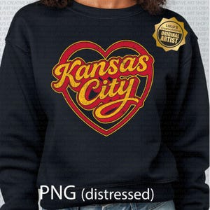 May include: Black sweatshirt featuring a distressed design of a red heart with the words "Kansas City" in yellow script. A gold "Original Artist" sticker is on the upper right. The bottom of the sweatshirt reads "PNG (distressed)".