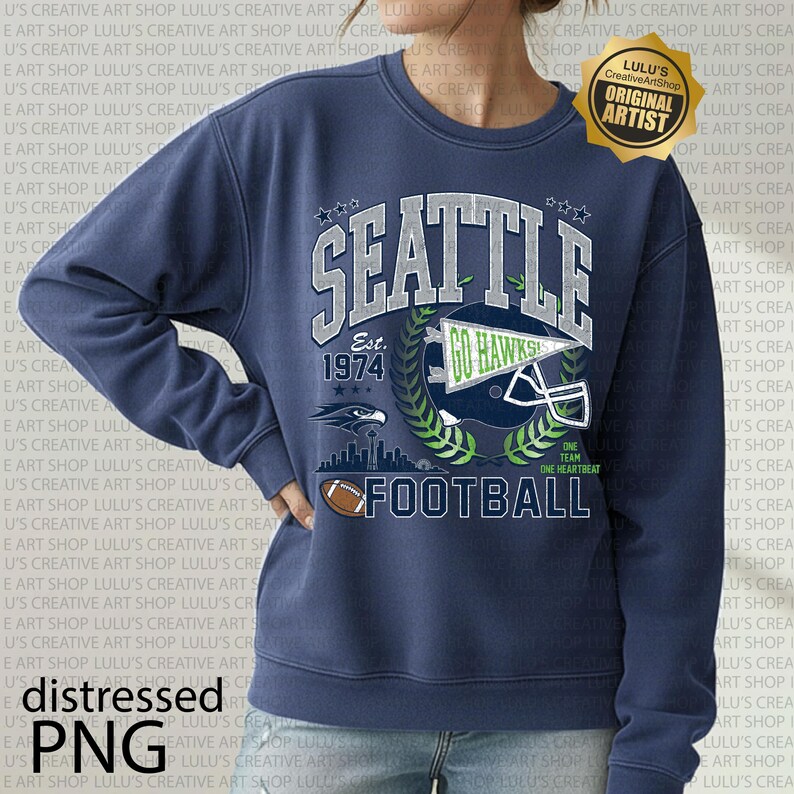 May include: Navy blue sweatshirt with a "SEATTLE FOOTBALL" graphic. The design includes a football helmet, the year "1974", and an eagle emblem. The sweatshirt has a distressed effect and a crew neck.