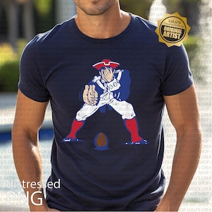 Op de afbeelding: Marineblauw t-shirt met een cartoon illustratie van een koloniale soldaat in witte en blauwe kleding, met rode laarzen en een steek. De soldaat poseert met een voetbal. Het shirt heeft een distressed PNG graphic.