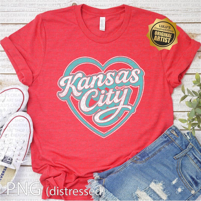 May include: Red t-shirt with a turquoise heart design that says "Kansas City" in white, distressed lettering. The shirt has rolled-up sleeves and is paired with denim shorts and white sneakers. A gold sticker reads "Lulu's Creative ArtShop Original Artist."