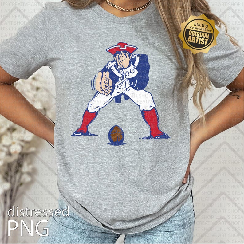 Op de afbeelding: Grijs t-shirt met een vervaagde afbeelding van een figuur uit de koloniale tijd in een patriottische outfit, poserend met een voetbal. Het ontwerp bevat rode, witte en blauwe kleuren. Het shirt heeft onderaan de tekst "distressed PNG".