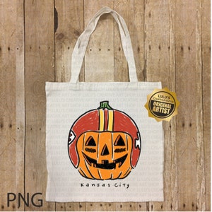 May include: White tote bag featuring a Halloween-themed design. The design includes an orange pumpkin wearing a red football helmet with yellow stripes. The words "Kansas City" are printed below the pumpkin.