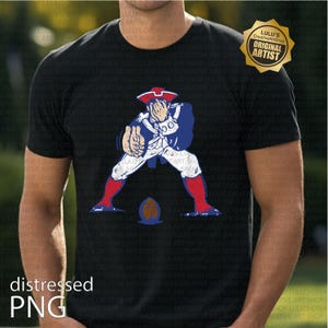 Op de afbeelding: Zwart T-shirt met een verweerde afbeelding van een koloniale figuur in blauw, wit en rood, met een voetbal. Het shirt heeft de tekst "distressed PNG" en een gouden "Original Artist" zegel.