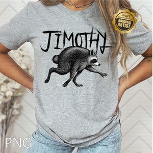 May include: A heather gray short-sleeve t-shirt featuring a black ink-style illustration of a raccoon in a running pose. Above the raccoon, the text JIMOTHY is printed in a stylized, jagged black font. A gold star-shaped badge is in the corner.