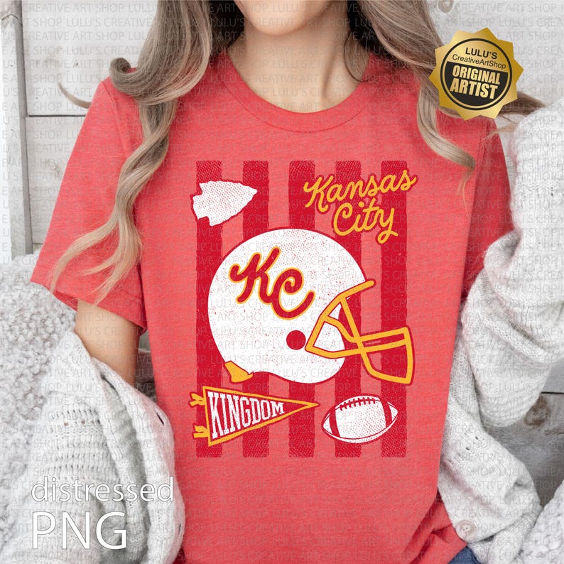 May include: A red short-sleeve t-shirt featuring a graphic print with vertical stripes, a white football helmet with the letters KC, a football, a pennant with the word KINGDOM, an arrowhead shape, and the text Kansas City in yellow script.