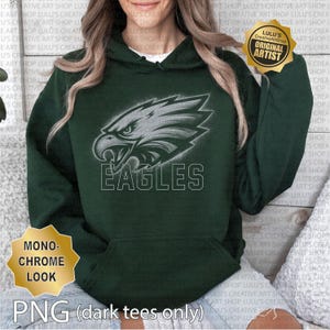May include: A dark green hoodie with a monochrome eagle head design and the word "EAGLES" in white. The hoodie has a hood with a drawstring and a front pocket. The image also includes text that says "MONOCHROME LOOK" and "PNG (dark tees only)".