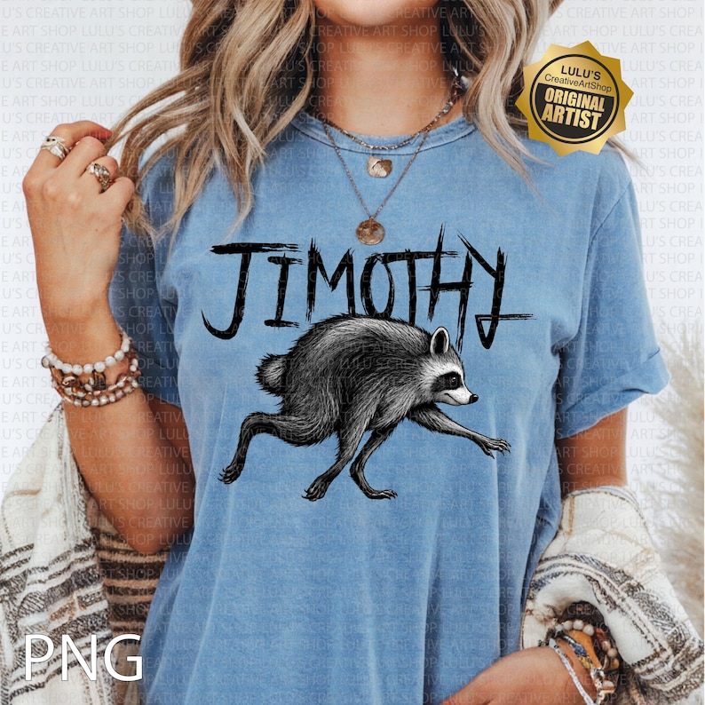 May include: A blue short-sleeve t-shirt featuring a black graphic illustration of a raccoon in a running pose. Above the raccoon, the text JIMOTHY is printed in a stylized, jagged black font. The shirt has a crew neckline and a washed-out appearance.