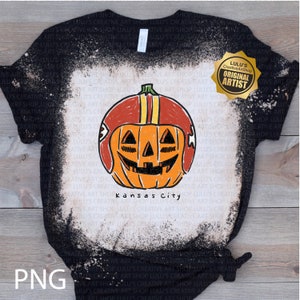 May include: Black t-shirt with a distressed bleach effect, featuring a hand-drawn pumpkin wearing a football helmet. The pumpkin has a carved face and the text "Kansas City" below. A gold seal reads "Original Artist".