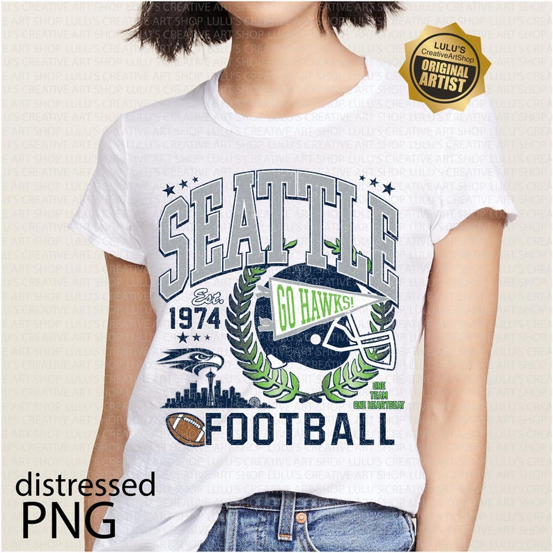 May include: White t-shirt with a distressed graphic design. The design includes the word "SEATTLE" in grey and blue, a football helmet, the text "GO HAWKS!", and the word "FOOTBALL". The shirt also features the text "Est. 1974".