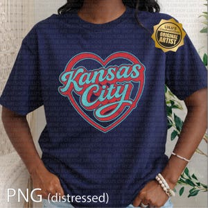 May include: Navy blue t-shirt featuring a distressed heart design with the text "Kansas City" in red and turquoise. The shirt includes the text "Lulu's Creative Art Shop" and "Original Artist" on a gold sticker.