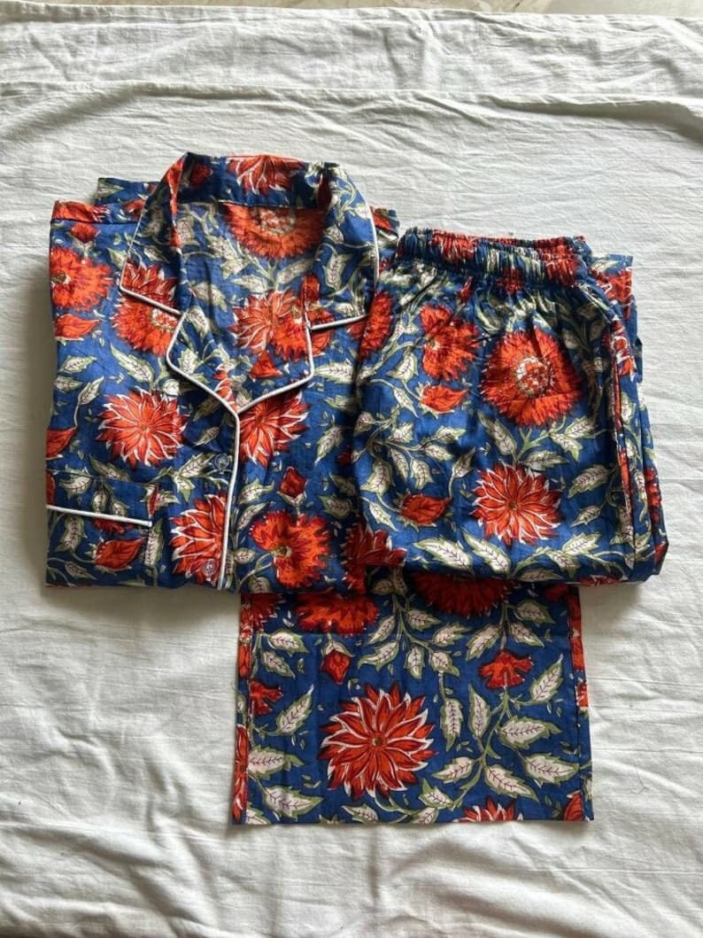 May include: A blue and red floral print pajama set with a white trim. The top has a button-up front and a collar. The pants have an elastic waistband.