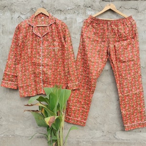 K&ouml;nnte beinhalten: Ein rot-braunes Pyjama-Set mit einem lang&auml;rmeligen Oberteil und einer Hose. Das Oberteil hat einen Knopfleisten vorne und einen wei&szlig;en Saum. Die Hose hat einen elastischen Bund und einen Kordelzug.