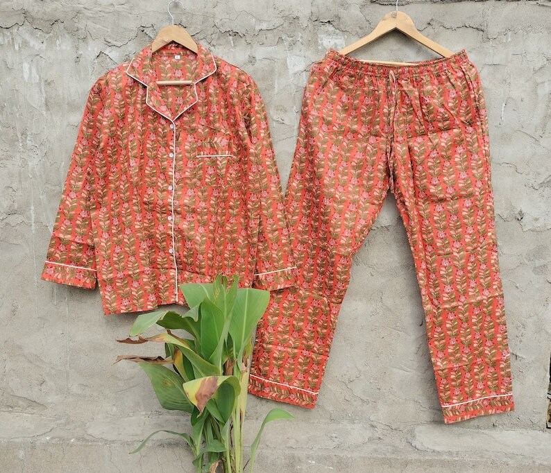 K&ouml;nnte beinhalten: Ein rot-braunes Pyjama-Set mit einem lang&auml;rmeligen Oberteil und einer Hose. Das Oberteil hat einen Knopfleisten vorne und einen wei&szlig;en Saum. Die Hose hat einen elastischen Bund und einen Kordelzug.