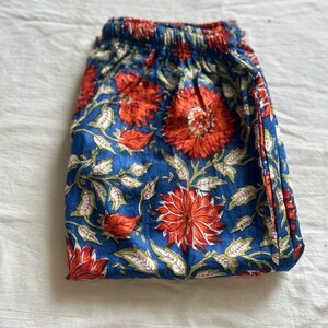 May include: A pair of blue cotton pants with a floral print in shades of orange and green. The pants have an elastic waistband.