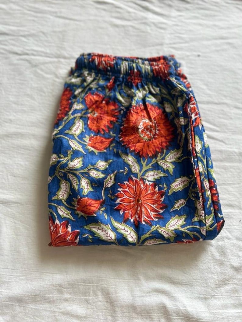 May include: A pair of blue cotton pants with a floral print in shades of orange and green. The pants have an elastic waistband.