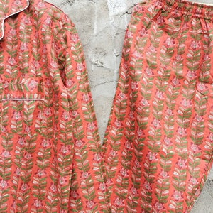 K&ouml;nnte beinhalten: Ein Pyjama-Set mit rotem und gr&uuml;nem Blumendruck und wei&szlig;em Besatz. Das Oberteil hat einen Knopfleisten vorne und lange &Auml;rmel. Die Hose hat einen elastischen Bund.