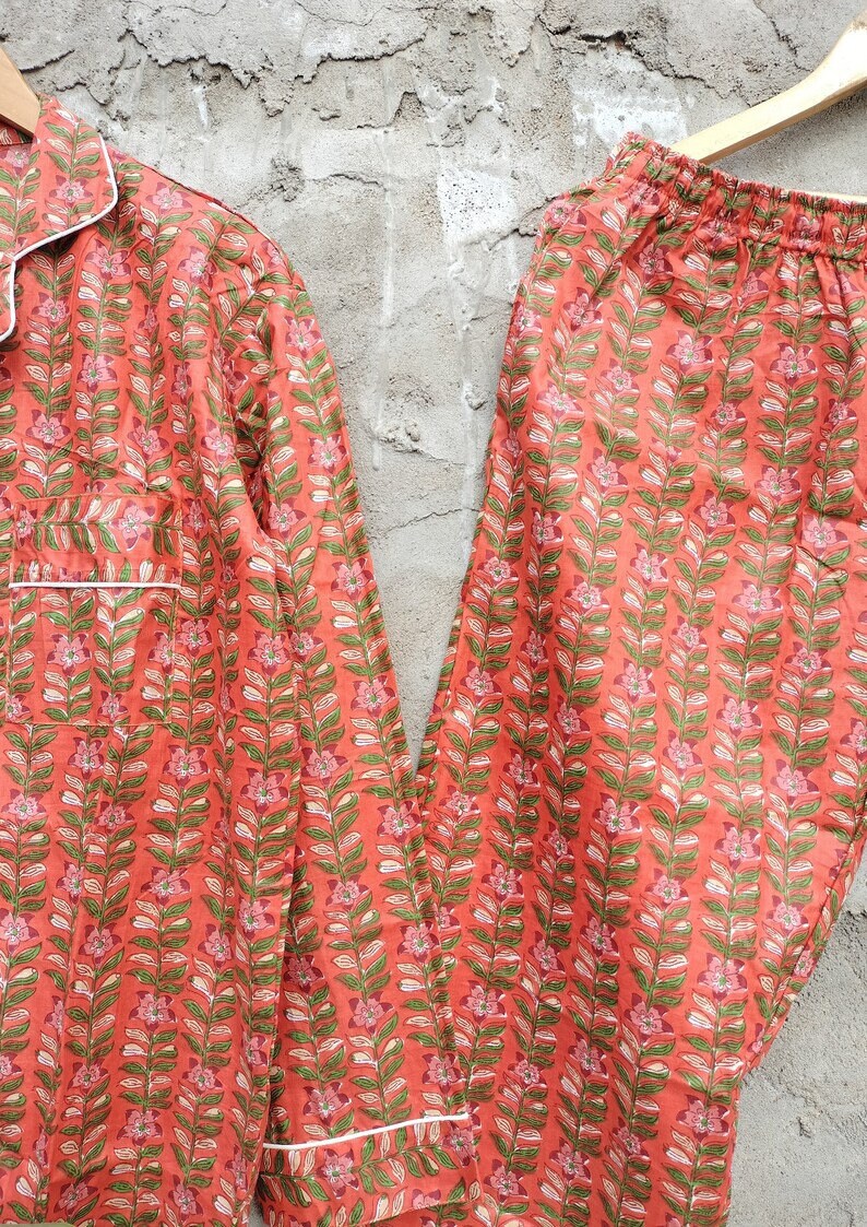 K&ouml;nnte beinhalten: Ein Pyjama-Set mit rotem und gr&uuml;nem Blumendruck und wei&szlig;em Besatz. Das Oberteil hat einen Knopfleisten vorne und lange &Auml;rmel. Die Hose hat einen elastischen Bund.