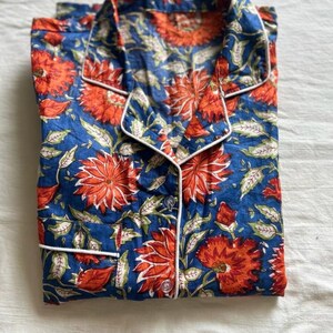 May include: A blue and orange floral print pajama top with white piping around the collar and button placket.