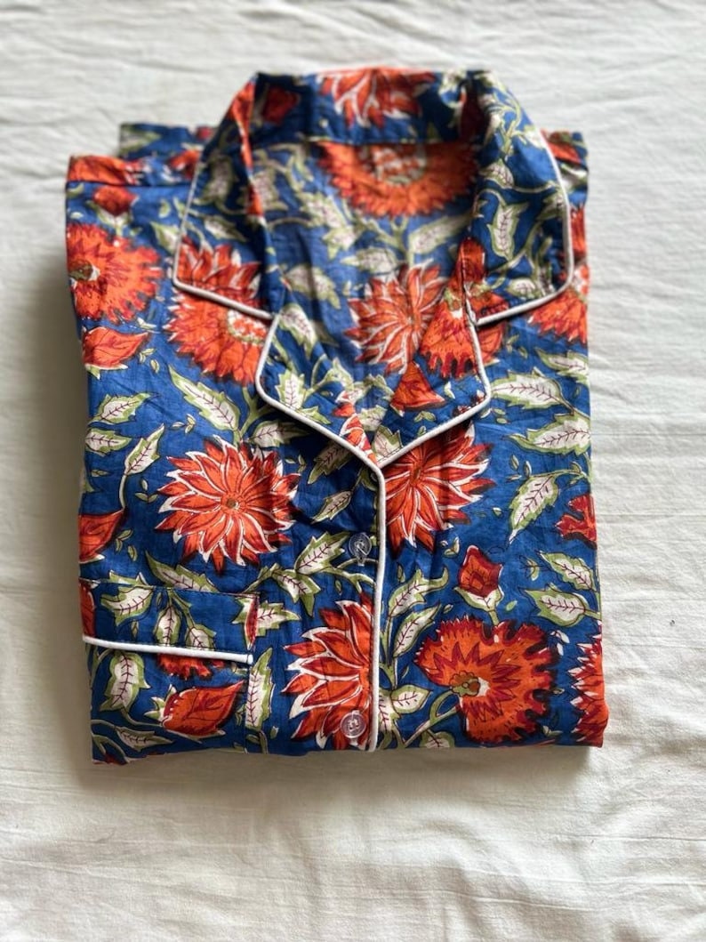May include: A blue and orange floral print pajama top with white piping around the collar and button placket.