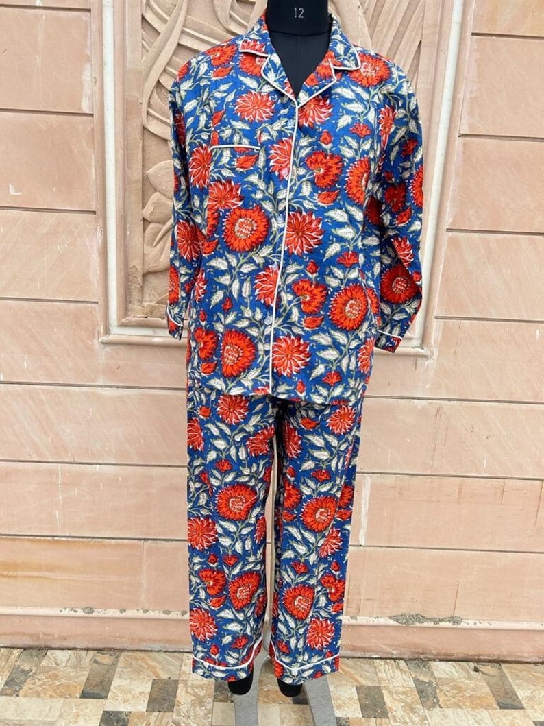 May include: Blue and red floral print pajama set with white piping. The top has a button-up front and long sleeves. The pants have a straight leg.