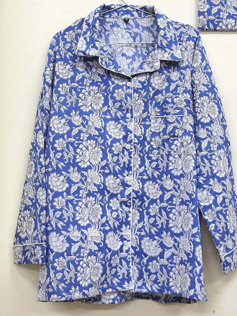 May include: A blue and white floral print long-sleeved shirt with a white trim around the collar and cuffs. The shirt has a button-up front.