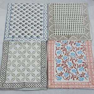 Puede incluir: Cuatro servilletas de algodón blanco con diferentes diseños impresos en bloque. Los diseños incluyen un patrón floral, un patrón geométrico, un patrón paisley y un patrón a rayas.