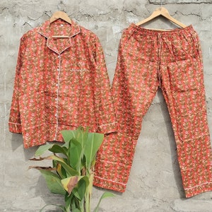 K&ouml;nnte beinhalten: Ein Pyjama-Set mit rotem und gr&uuml;nem Blumendruck, langen &Auml;rmeln und einer Hose. Der Pyjama hat einen wei&szlig;en Saum.