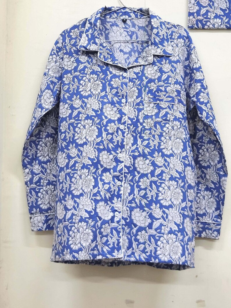 May include: A blue and white floral print long-sleeved shirt with a button-up front and a white trim.
