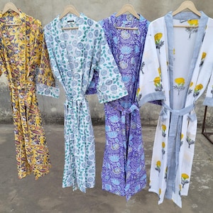 May include: Four colorful, patterned robes hanging on wooden hangers. The robes feature floral designs in yellow, blue, and purple. One robe is white with yellow flowers and blue stripes. Each robe has a matching belt.