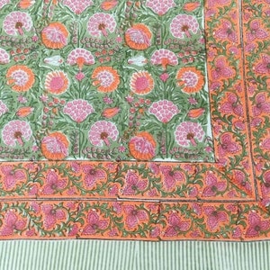 Puede incluir: Una tela de algodón verde y blanca con un estampado floral en tonos rosa y naranja. La tela tiene un borde con un patrón floral repetitivo.